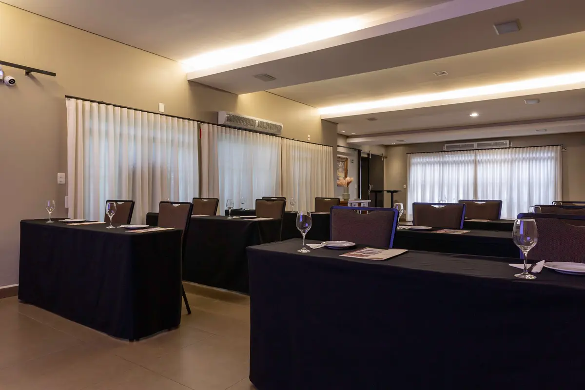 Auditório do Vivá montado em formato escolar, com mesas cobertas de preto e cortinas claras