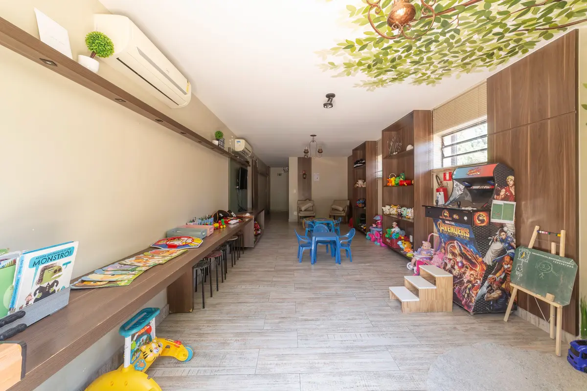 Brinquedoteca do Vivá com árvore pintada na parede, mesinhas e brinquedos