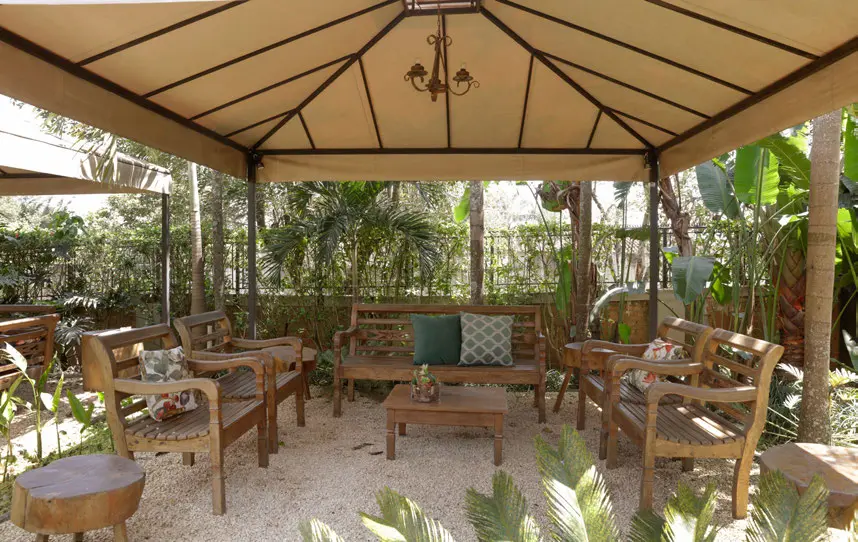 Gazebo com sofás de madeira e almofadas no meio da vegetação