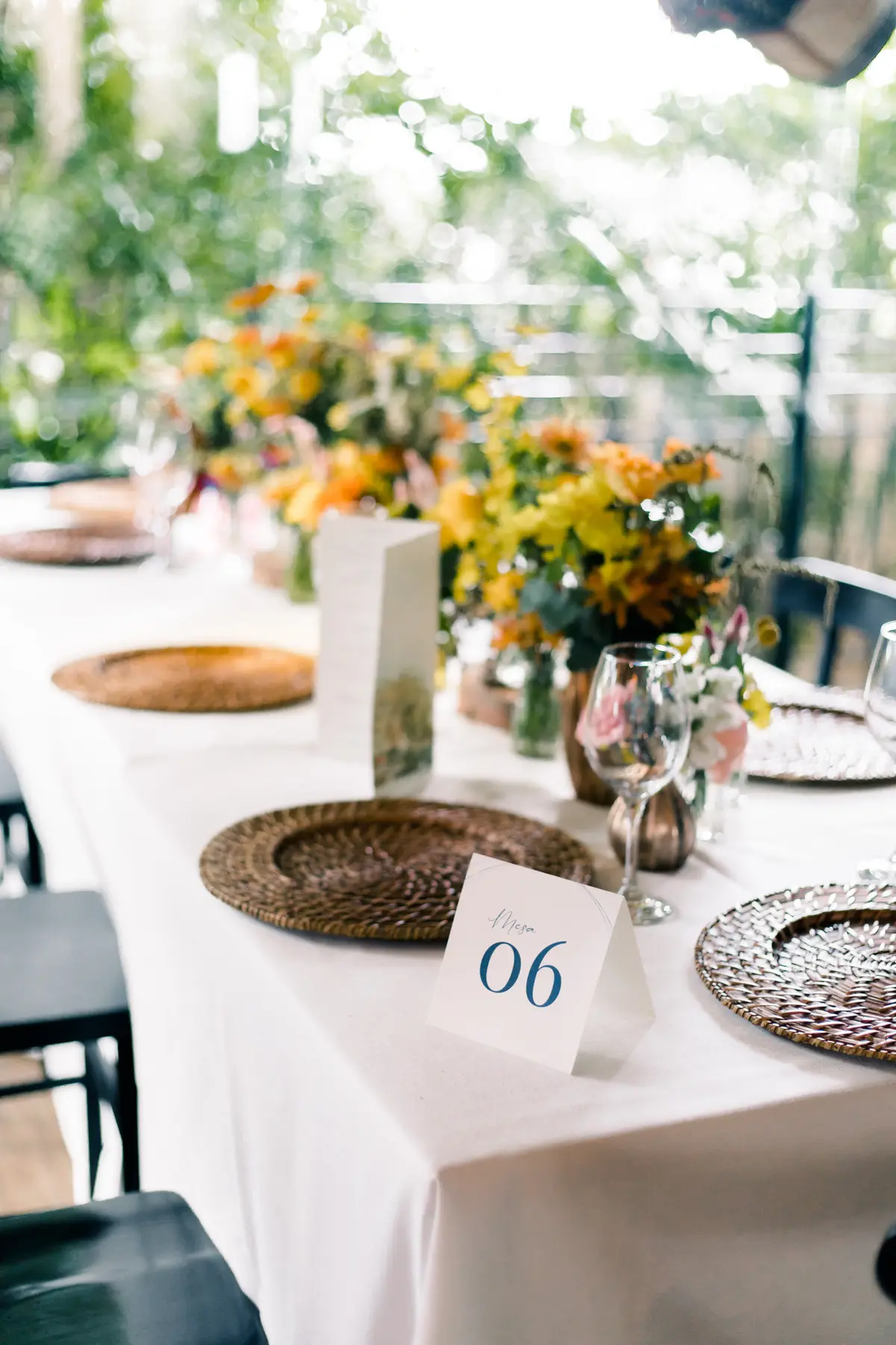 Mesa de evento com toalha branca, sousplat de palha e arranjo de flores laranja